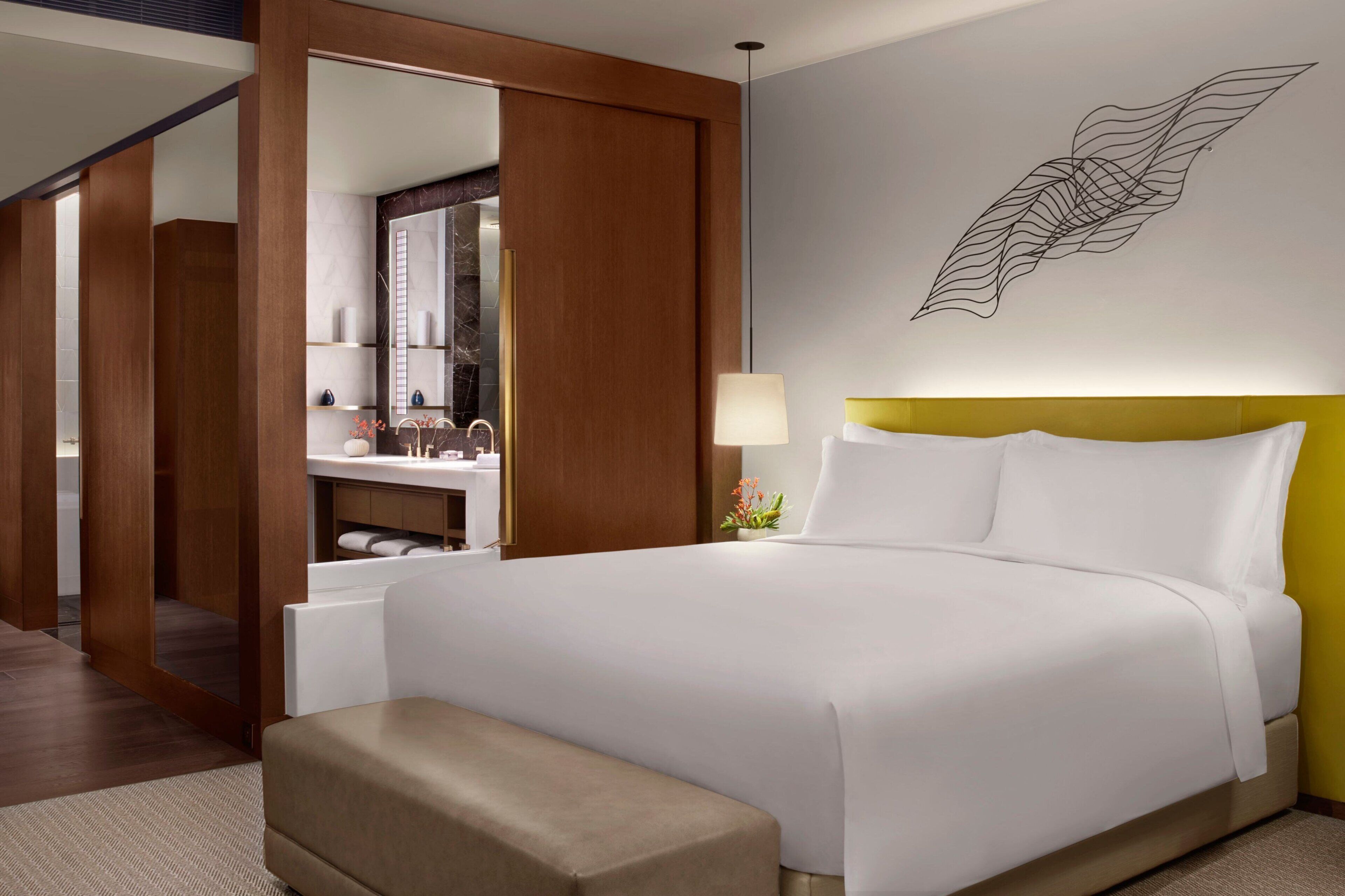 A hotel room with a large bed, a bedside table, a mirror, and a wall-mounted artwork.