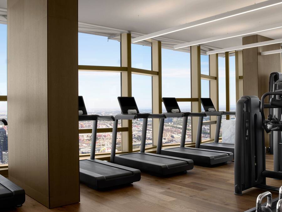Ein Fitnessstudio mit Laufbändern und Kraftgeräten, großen Fenstern und Blick auf eine Stadtlandschaft.