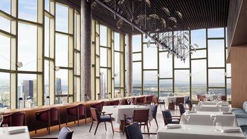 A high-rise restaurant with large windows offering city views, modern interior design, and a variety of seating arrangements.