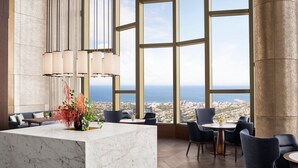 Een moderne hotellobby met een marmeren receptiebalie, comfortabele zitplaatsen, grote ramen met uitzicht over de stad en een hangende lamp.
