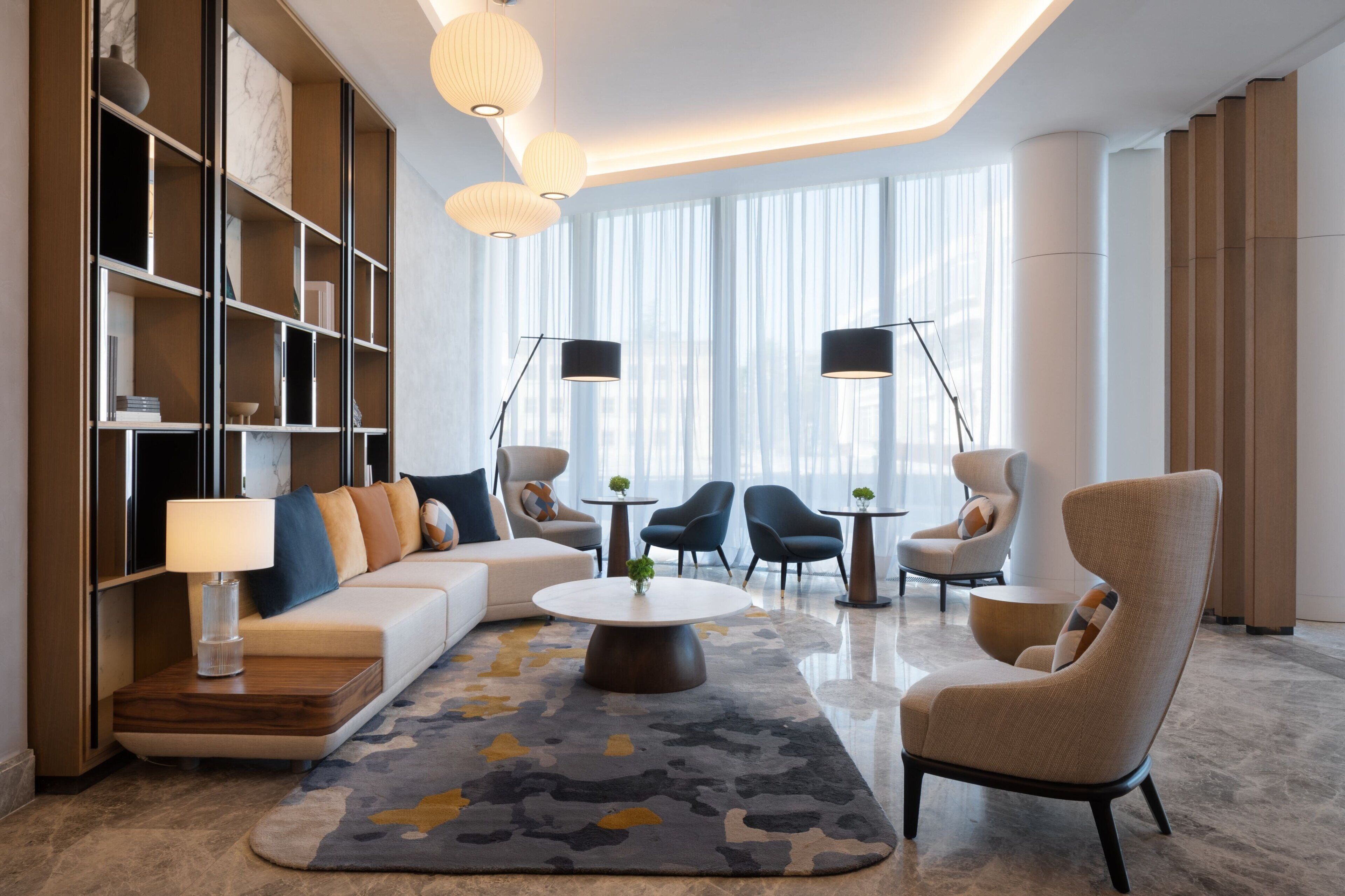 A modern hotel lobby with a sofa, armchairs, a coffee table, and a bookshelf.