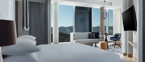 Habitación de hotel moderna con una cama grande, un sofá, un televisor y vistas a la montaña.