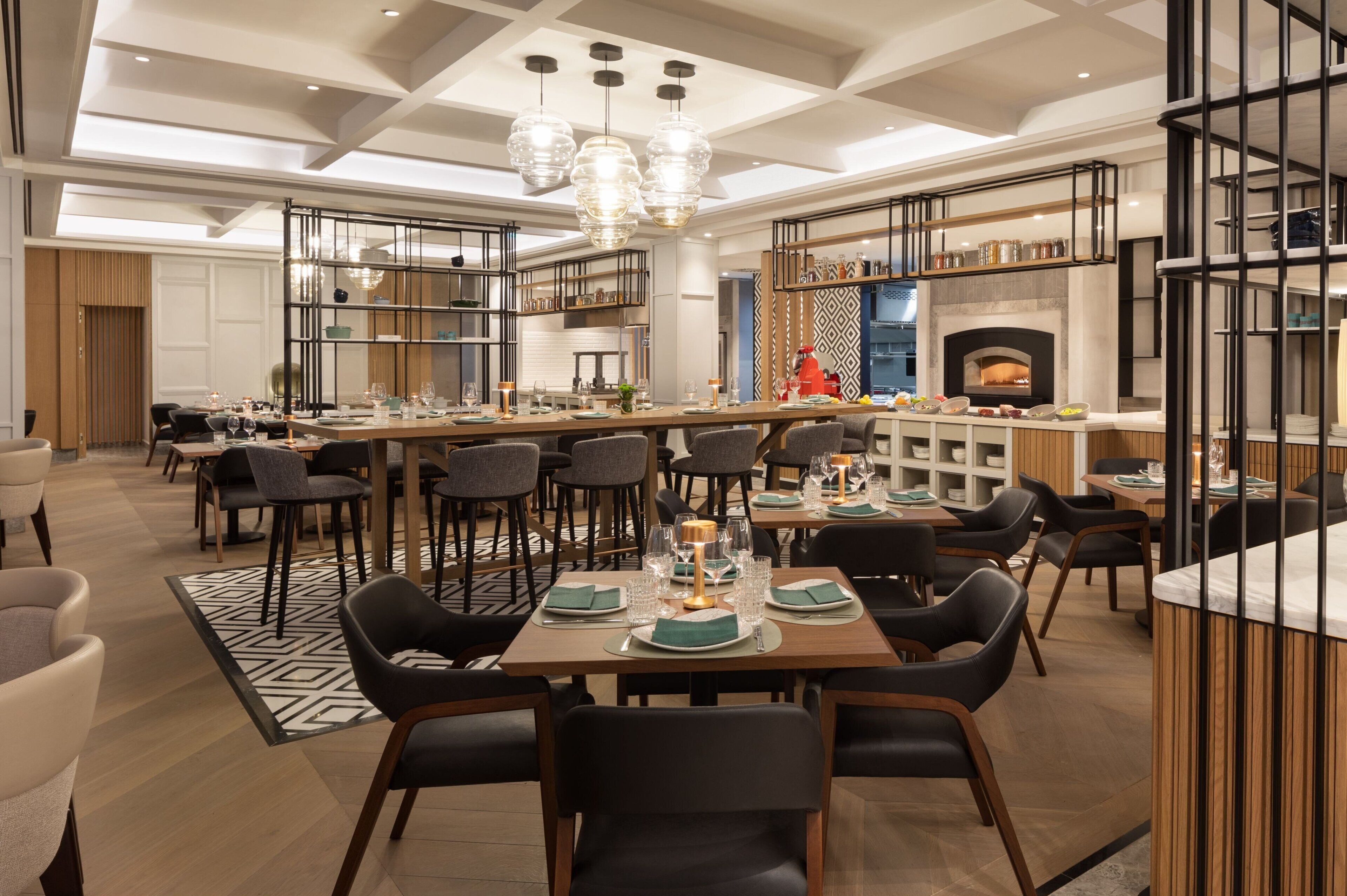 Un comedor moderno con varias mesas y sillas, una chimenea en el centro y una zona de cocina con estantes y una estufa.