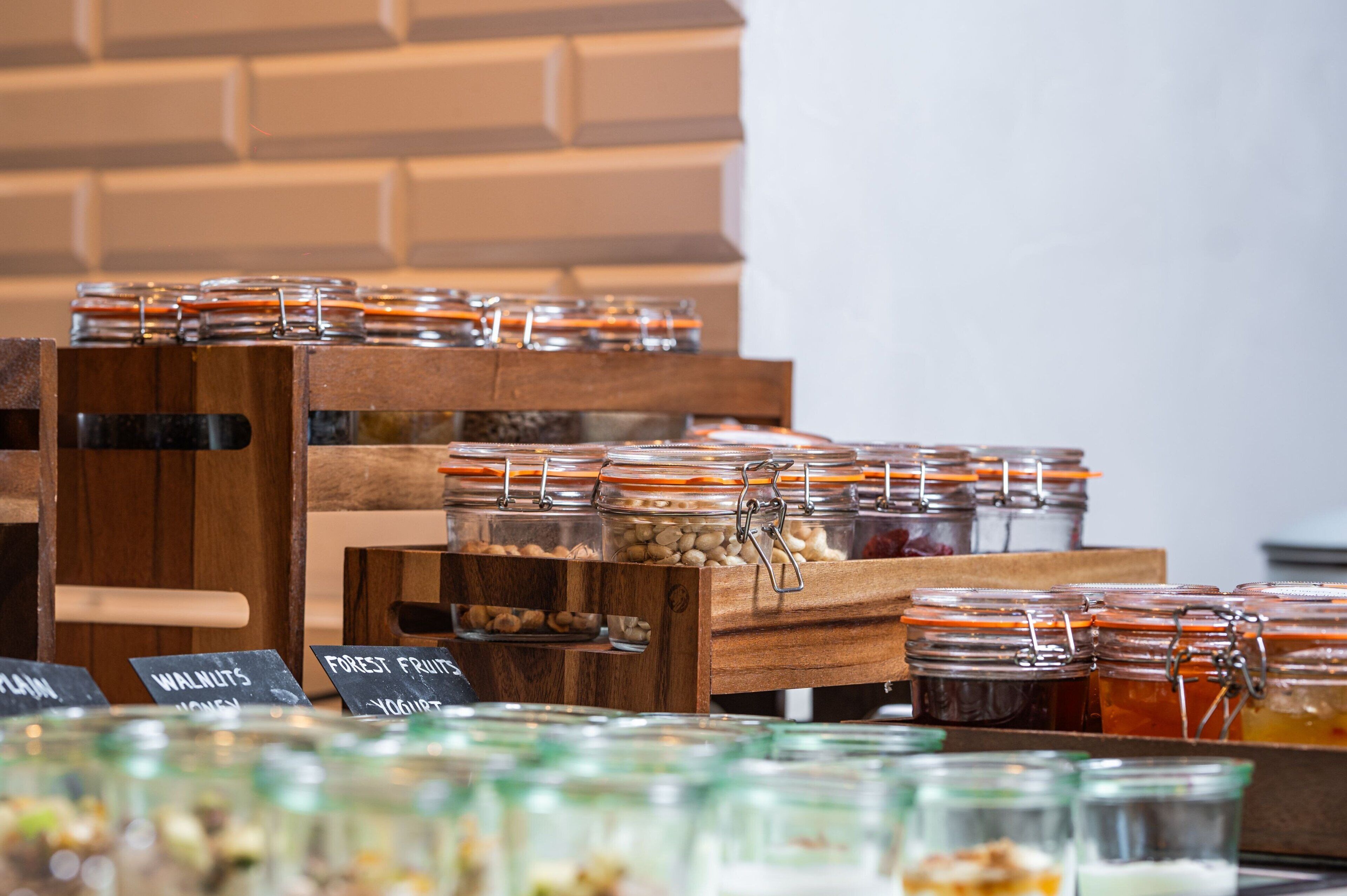 A display of various food items in glass jars with labels, arranged on wooden stands.