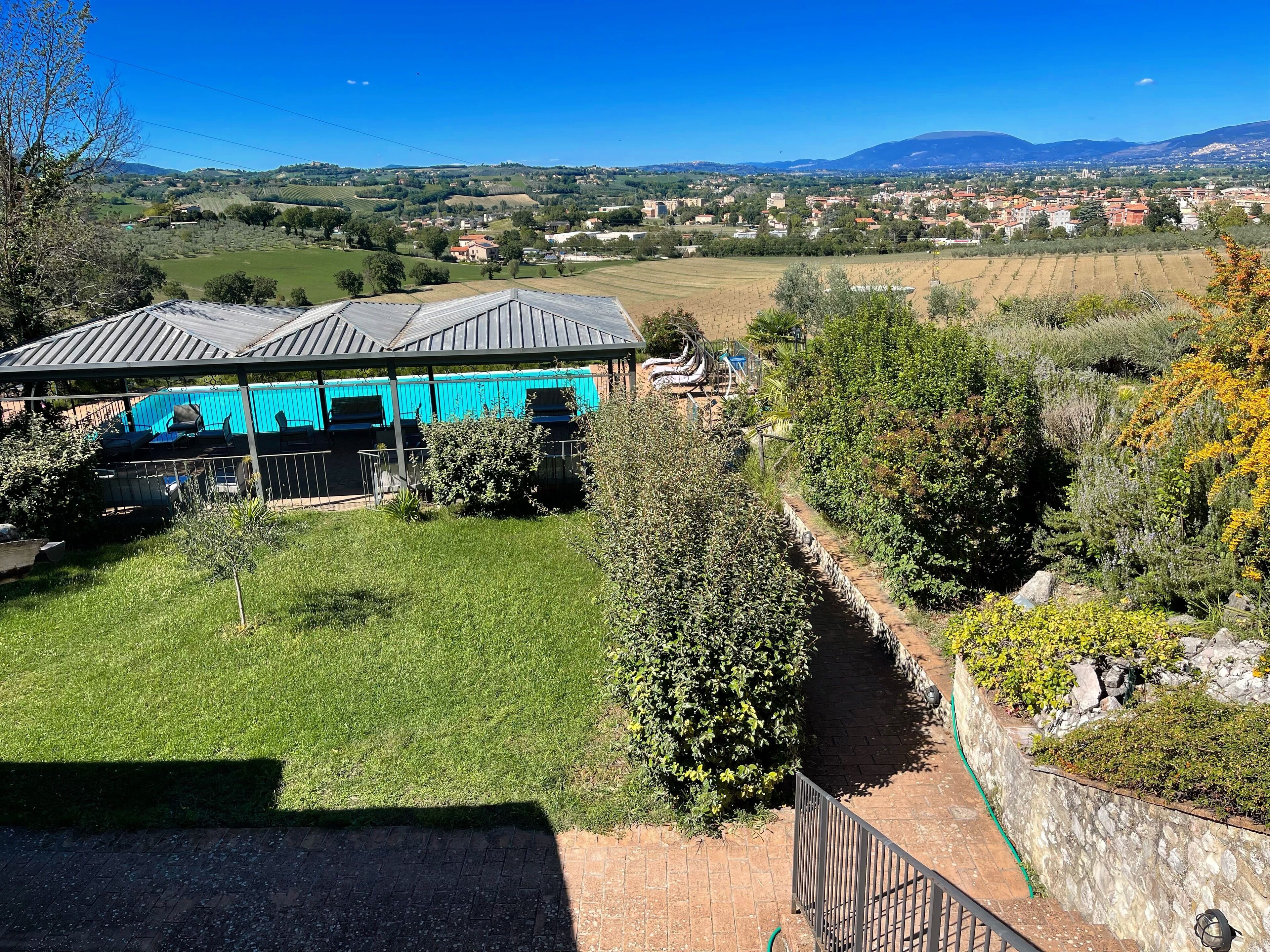 Vista de una propiedad con un área de estar al aire libre techada, un césped bien cuidado y un sendero de piedra que conduce a un edificio con techo azul.