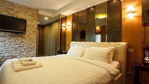A hotel room with a large bed, a flat-screen TV mounted on a textured wall, and a mirror with integrated lighting. - 2D - 3 Bedroom Downtown Apartment With Shared Pool (Bangkok)