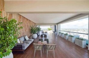 A modern outdoor lounge area with a wooden floor, seating arrangements, and potted plants. - Luxury Condo 1 Br Pool Excellent Location (Santo Domingo)