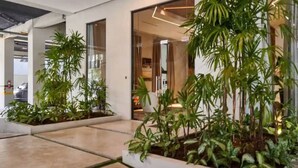 A modern indoor space with a concrete floor, potted plants, and a glass door leading to a room with a bed and curtains. - Luxury Condo 1 Br Pool Excellent Location (Santo Domingo)