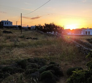 Paisaje rural con un atardecer, muros de piedra y edificios blancos.