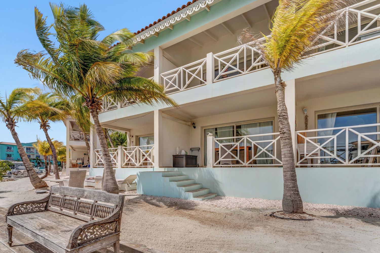 A beachfront hotel with a two-story structure, outdoor seating, and palm trees.