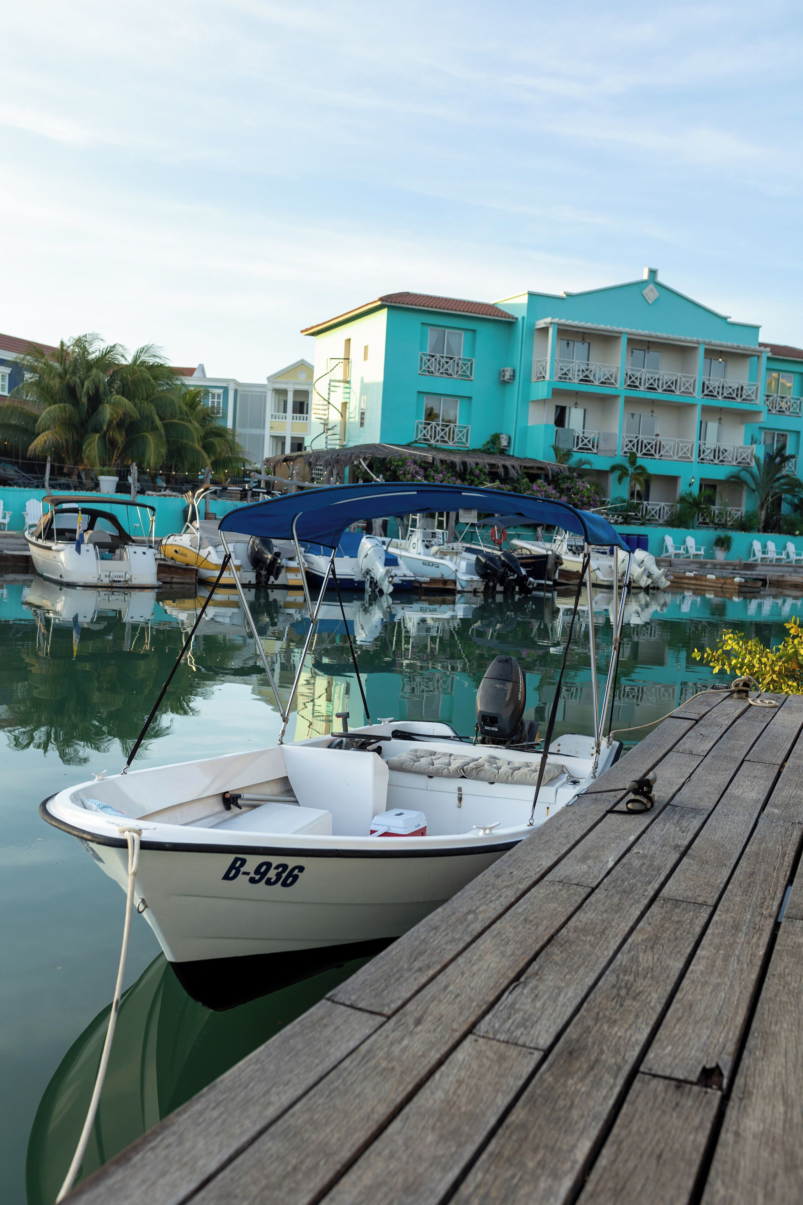 A marina with boats docked, a wooden pier, and a turquoise building with balconies.