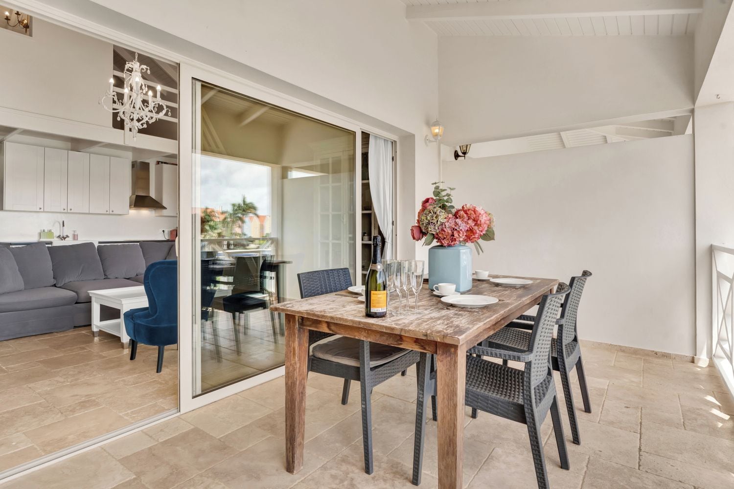 A dining area with a wooden table, chairs, a vase with flowers, and a bottle of wine.