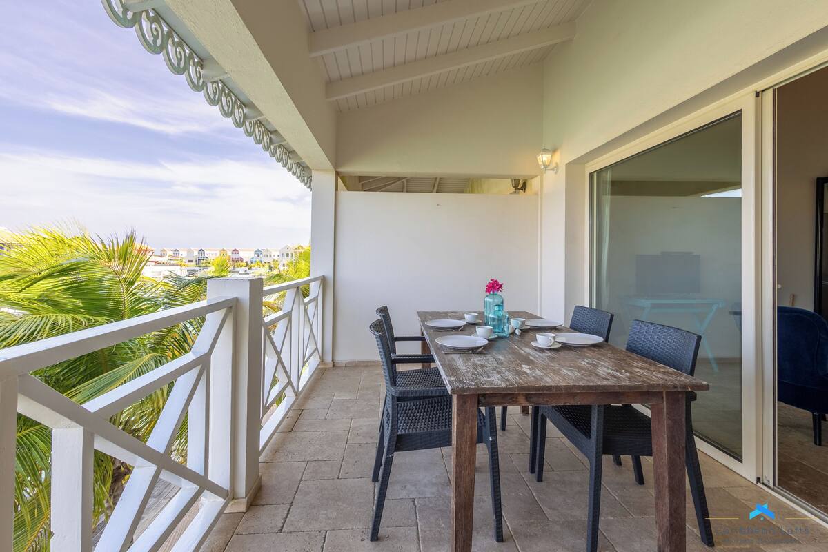 Ein Balkon mit Tisch und Stühlen, Blick auf die Stadt und eine Glastür zu einem Innenbereich.