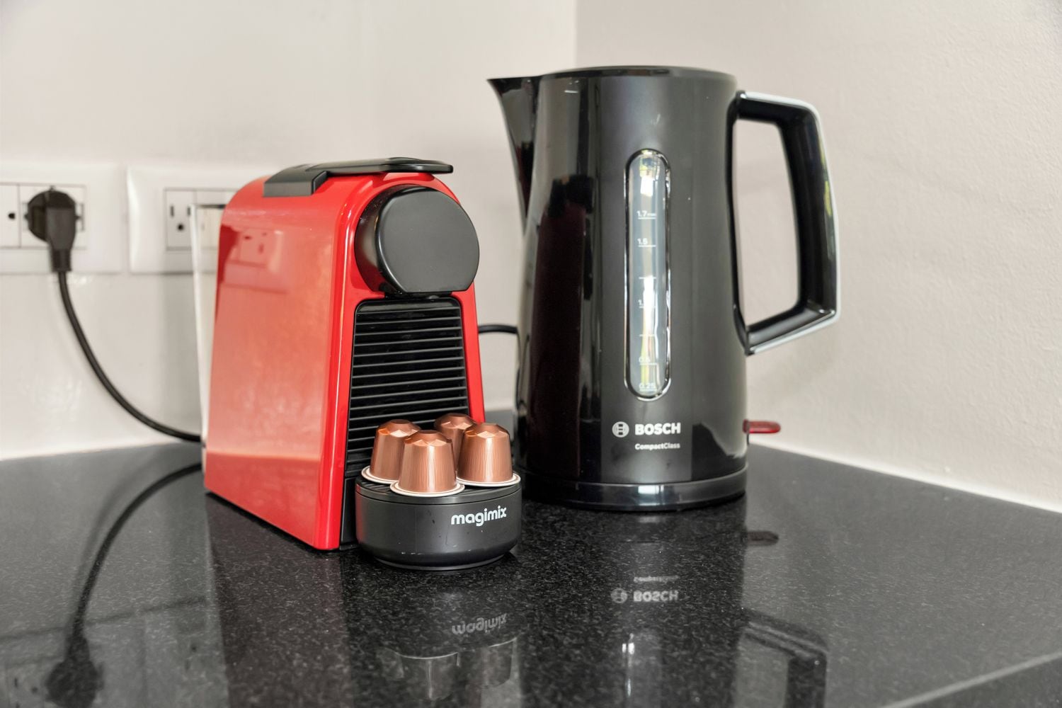 Una cafetera roja y negra con cuatro tazas y un hervidor Bosch negro sobre una encimera.