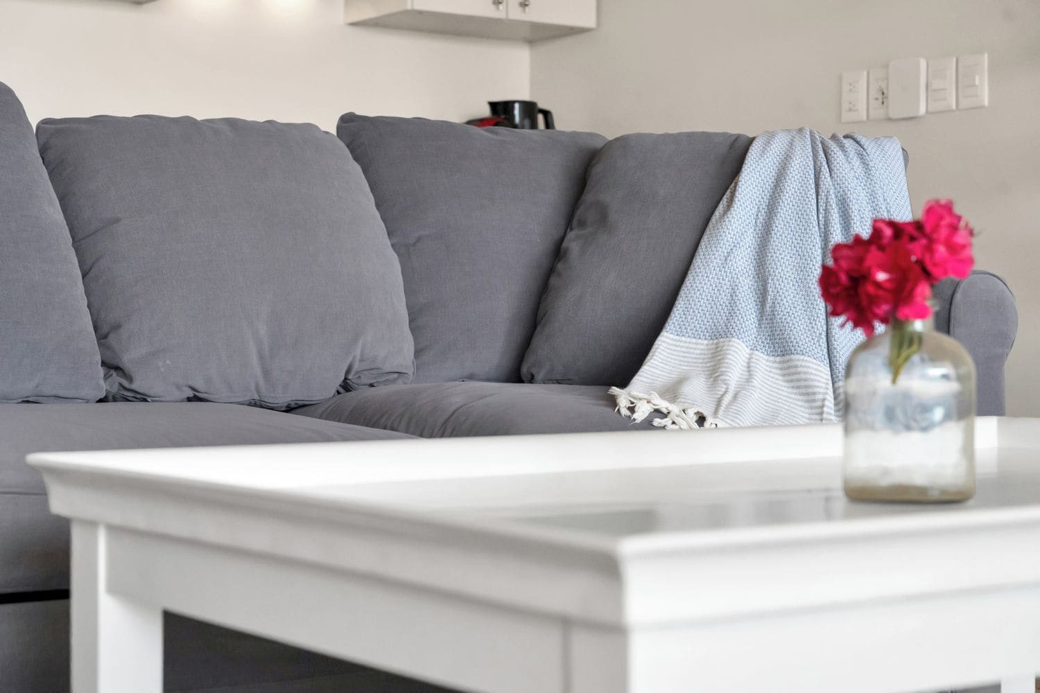 A modern living room with a grey sofa, a white coffee table, and a vase with flowers.