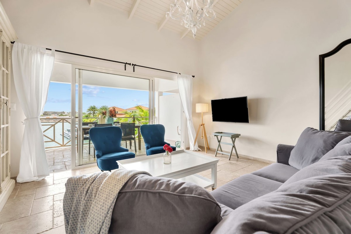 A living room with a sofa, two armchairs, a coffee table, a flat-screen TV, and a view of the outdoors through a sliding glass door.