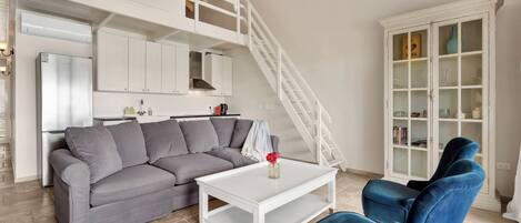 Una sala moderna con un sofá seccional gris, una mesa de centro blanca y un sillón azul. Una escalera blanca conduce a un nivel superior.