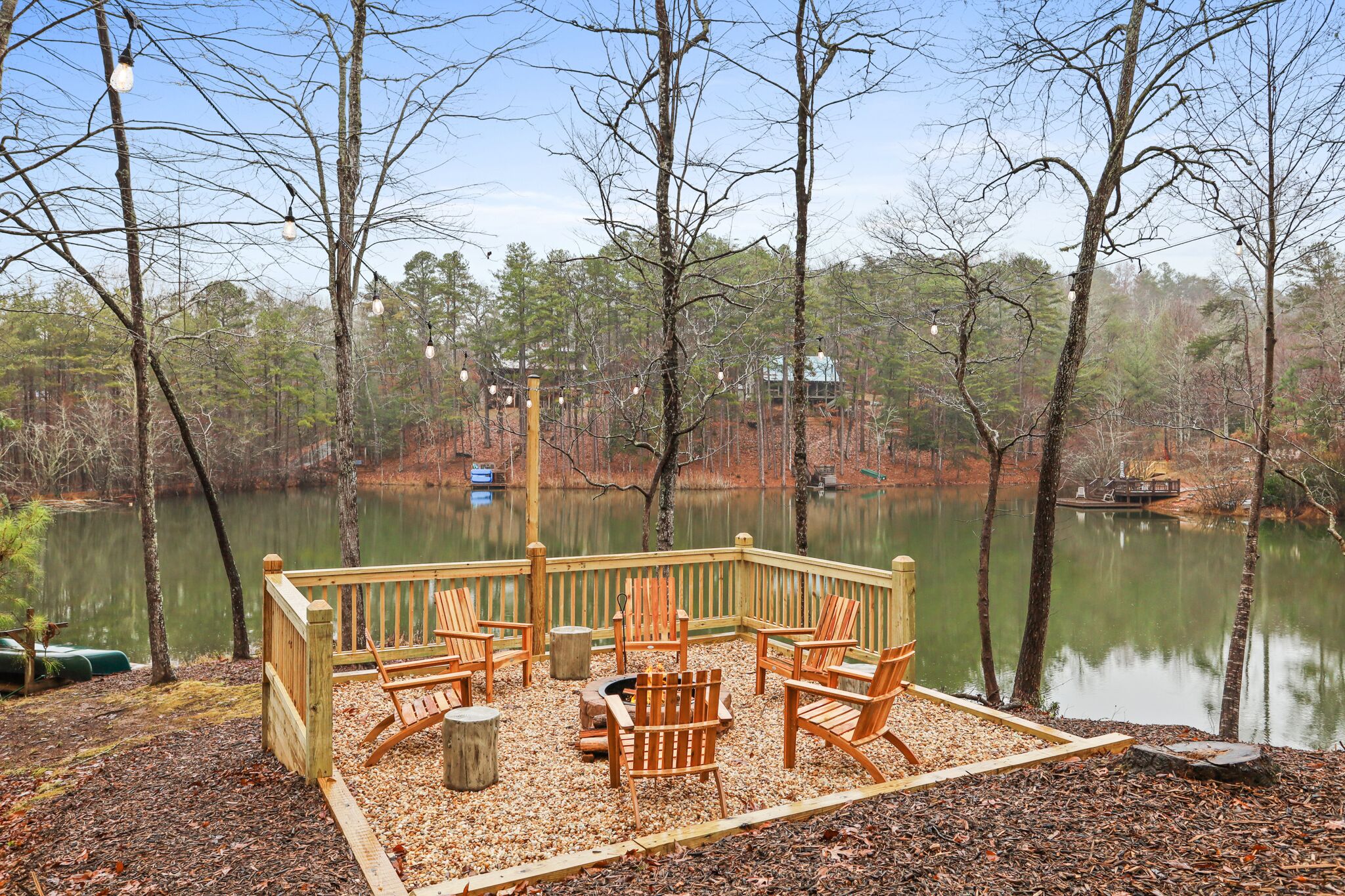 A wooden deck with Adirondack chairs overlooking a lake, surrounded by trees.