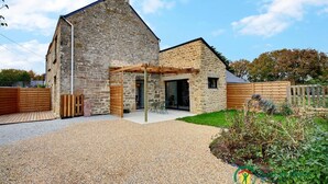 Una casa in pietra con vialetto sterrato, recinzione in legno e giardino.