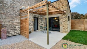 Un edificio in pietra con una pergola in legno, una porta in vetro e un piccolo patio con sedie.