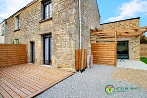 Un bâtiment en pierre doté d’une terrasse en bois et d’un espace extérieur couvert.