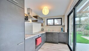 A modern kitchen with grey cabinets, a built-in oven, a sink, and a window overlooking a garden.