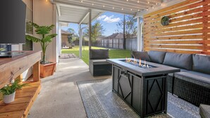 Een terras buiten met een vuurkorf, zitplaatsen en een televisie op een houten tafel.