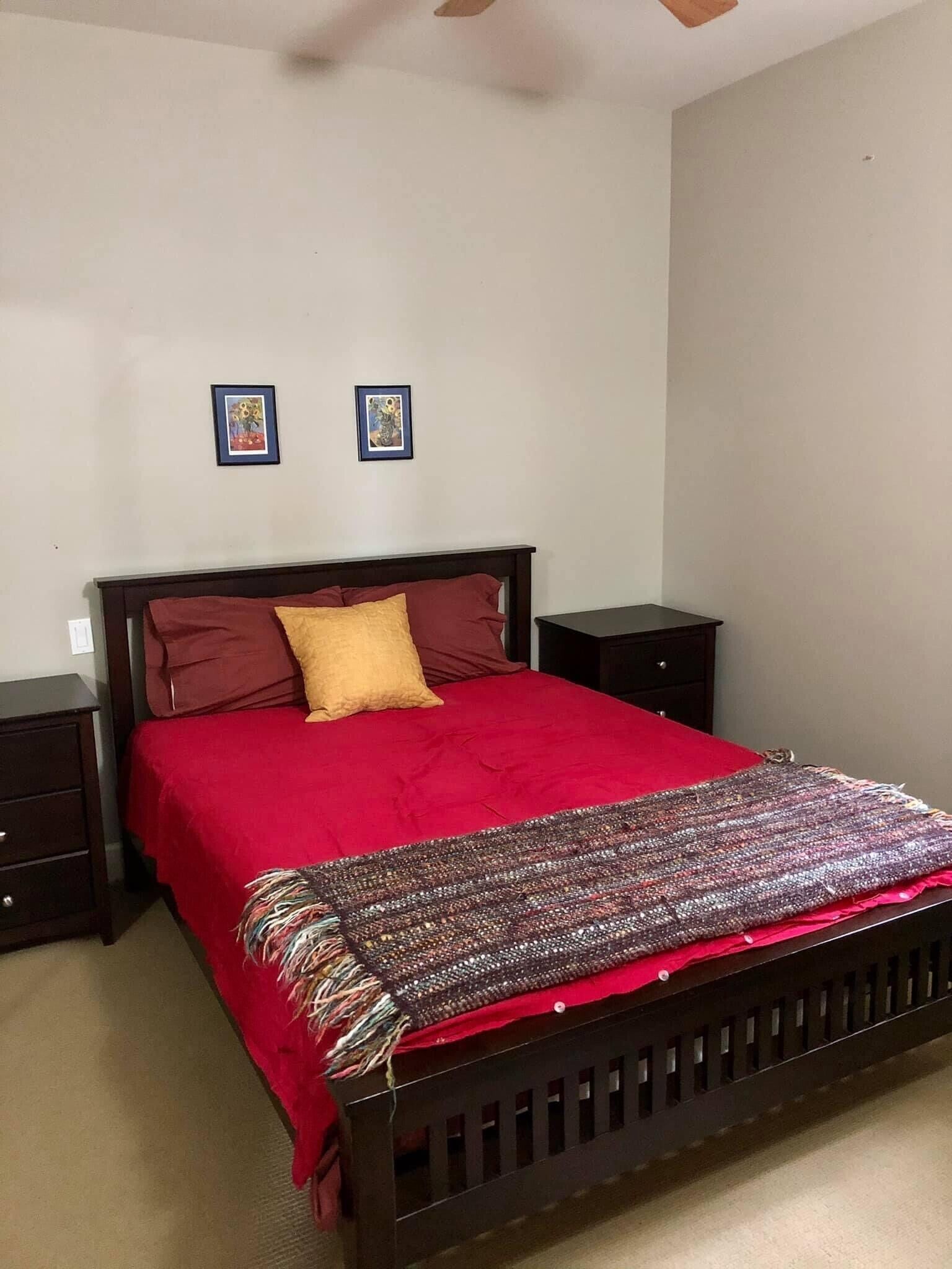 A bedroom with a wooden bed, red bedding, two nightstands, and two framed pictures on the wall.