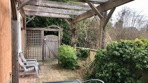 Un patio techado con mesa y sillas, una reja de madera y follaje circundante.