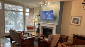 Una sala de estar con chimenea, un televisor colocado encima y una mesa de vidrio.