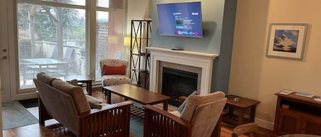 A living room with a fireplace, a television mounted above it, and a glass table.