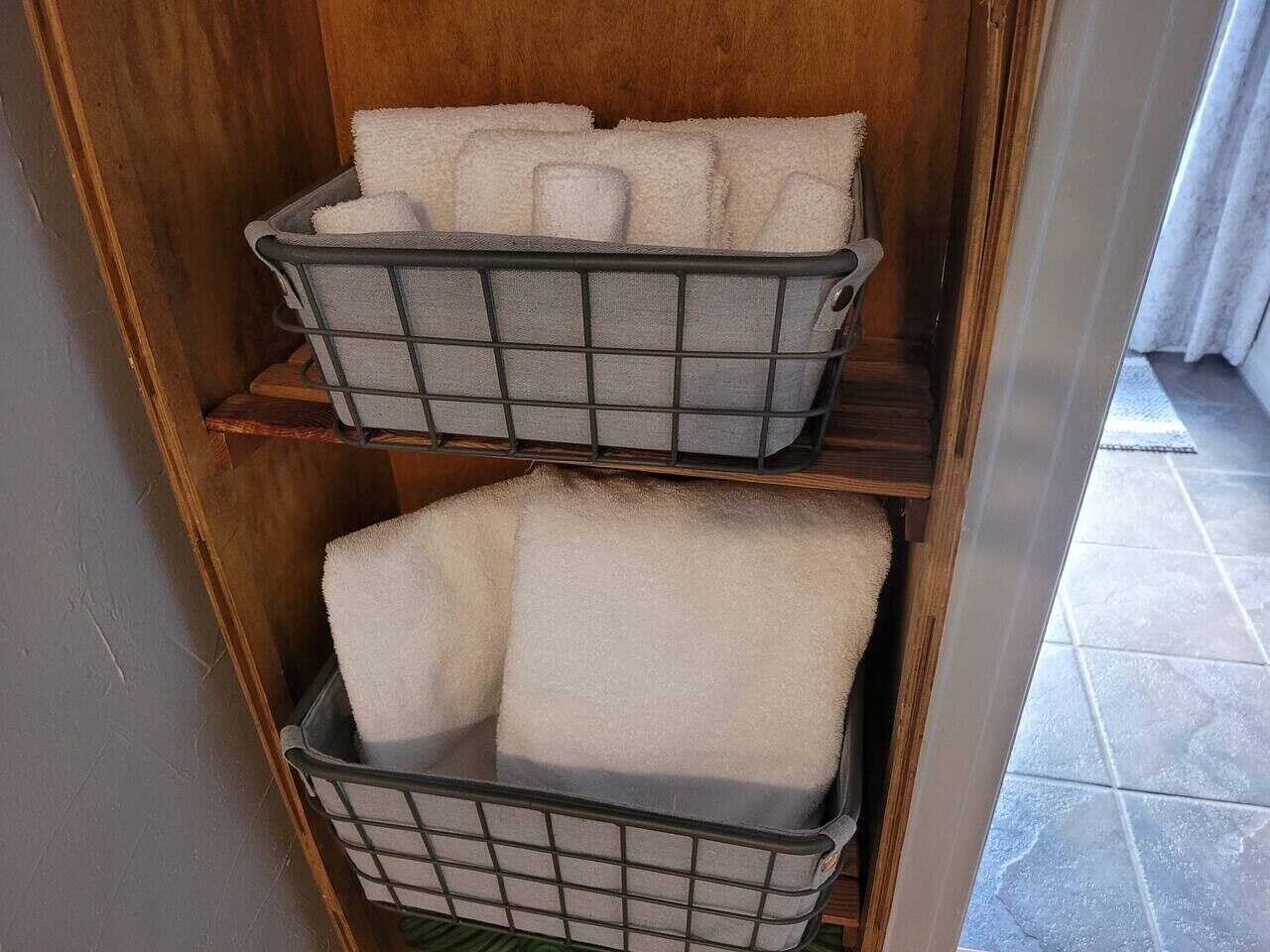 Zwei Drahtkörbe mit gefalteten Handtüchern auf Holzböden.