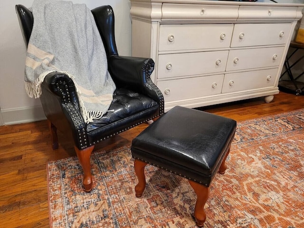 A black leather armchair with a patterned throw blanket, a matching ottoman, and a white dresser with multiple drawers.