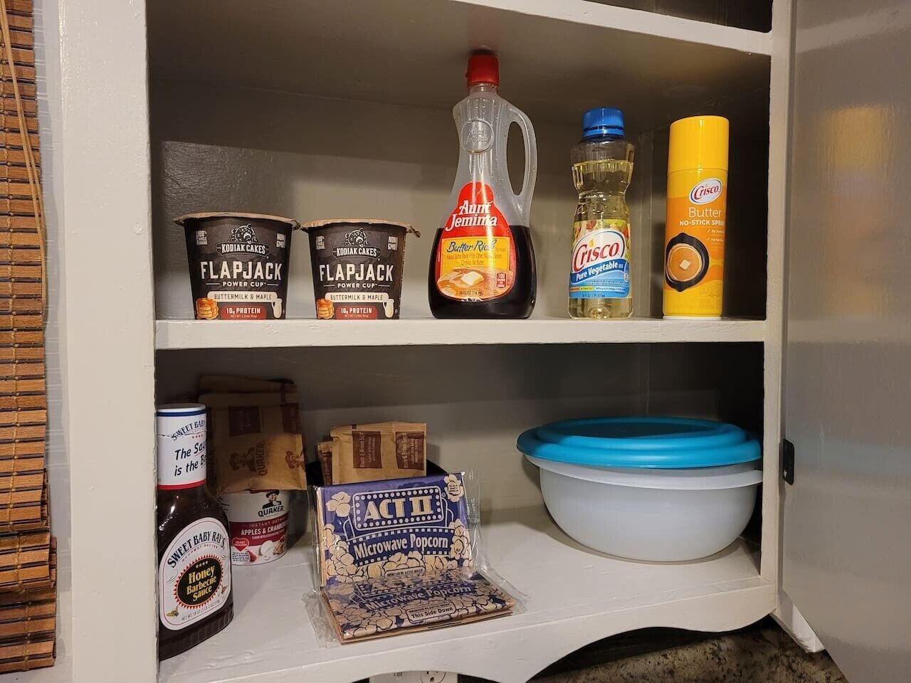 A pantry with various food items including sweet baby rice syrup, microwave popcorn, and a large blue bowl.