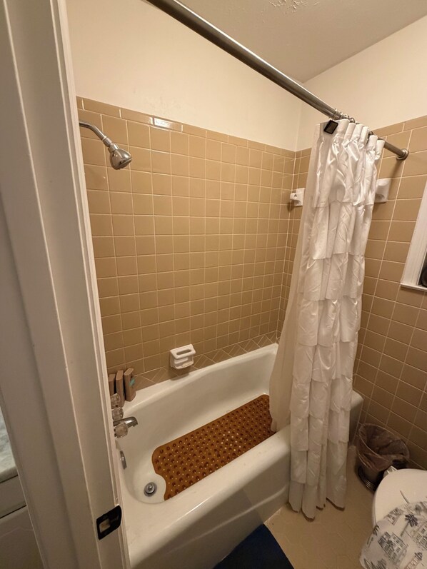 A bathroom with a bathtub, a shower curtain, and a tiled wall.