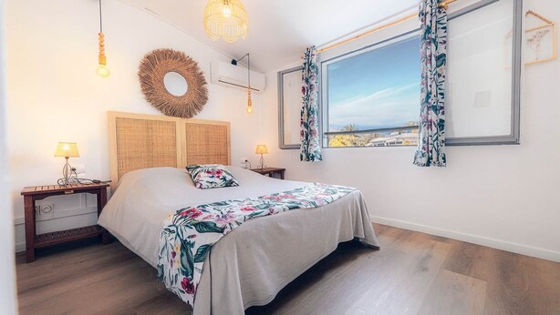 Ein Schlafzimmer mit einem Bett, zwei Nachttischen, einem Fenster mit Vorhängen, einer Wandleuchte und einer gewebten Wanddekoration.