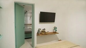 Ett sovrum med en säng, en tv som är monterad på väggen och en hylla med diverse föremål.