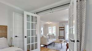 Ett rymligt rum med en stor säng, en soffa och ett soffbord. Det finns en dörr som leder till ett annat rum och ett fönster som släpper in naturligt ljus.