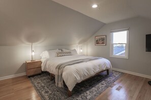 Un dormitorio con cama, mesitas de noche, alfombra, ventana y un cuadro en la pared.