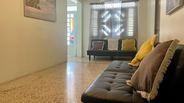 Ein Wohnzimmer mit einer schwarzen Ledersofa, einem Deckenventilator und einem Fenster mit gemusterten Vorhängen.