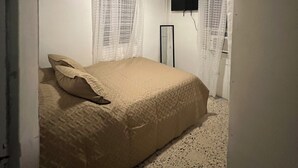 Ein Schlafzimmer mit einem Bett, einem Deckenventilator, einem an der Wand befestigten Fernseher und transparenten Vorhängen.
