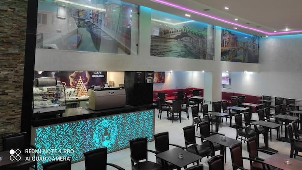 A restaurant with multiple tables and chairs, a counter with a coffee machine, and large windows with cityscape views. - Appartment with Moroccan breakfast (Dakhla)