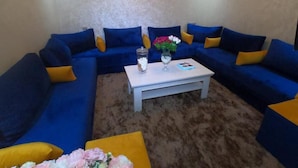 A living room with a blue sofa set, a white coffee table, and a vase with flowers. - Appartment with Moroccan breakfast (Dakhla)