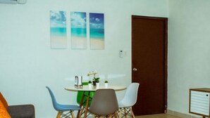 A living room with a grey sofa, a coffee table, and a dining area with a round table and four chairs. There are three framed pictures on the wall above the dining table. - 5 minutes from eagle beach as an apartment with kitchen and (Noord)