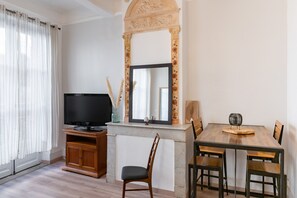 Een kamer met een televisie, een eettafel met stoelen, een houten kast en een grote spiegel met een bloemdecoratie.
