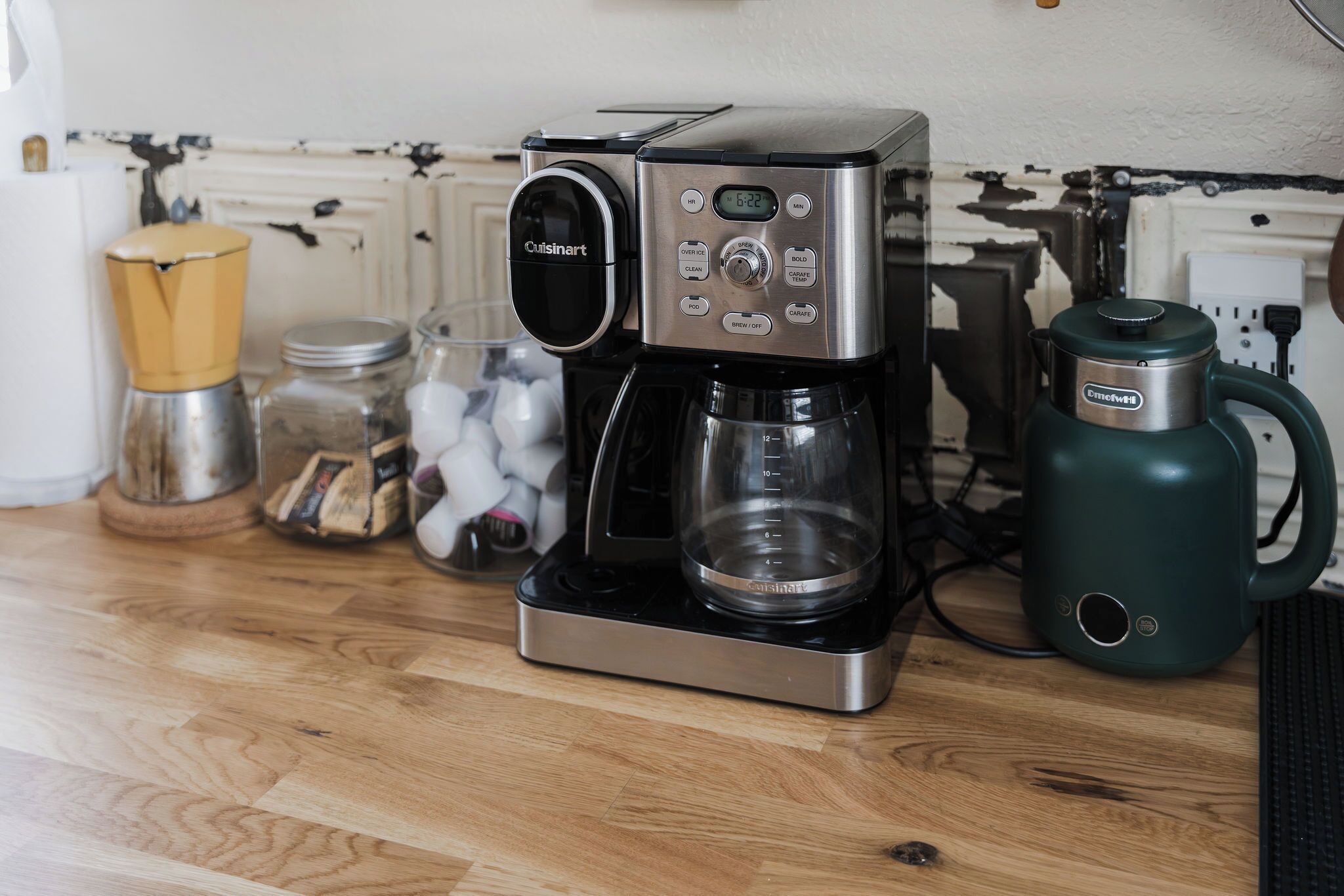 Cuisinart-kahvinkeitin puupintaisella työtasolla, sen vieressä vihreä sähköinen vedenkeitin ja lasipurkki, jossa on vanupuikkoja.