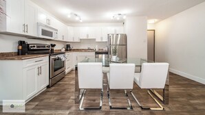 A modern kitchen with white cabinets, stainless steel appliances, and a glass dining table with white chairs.