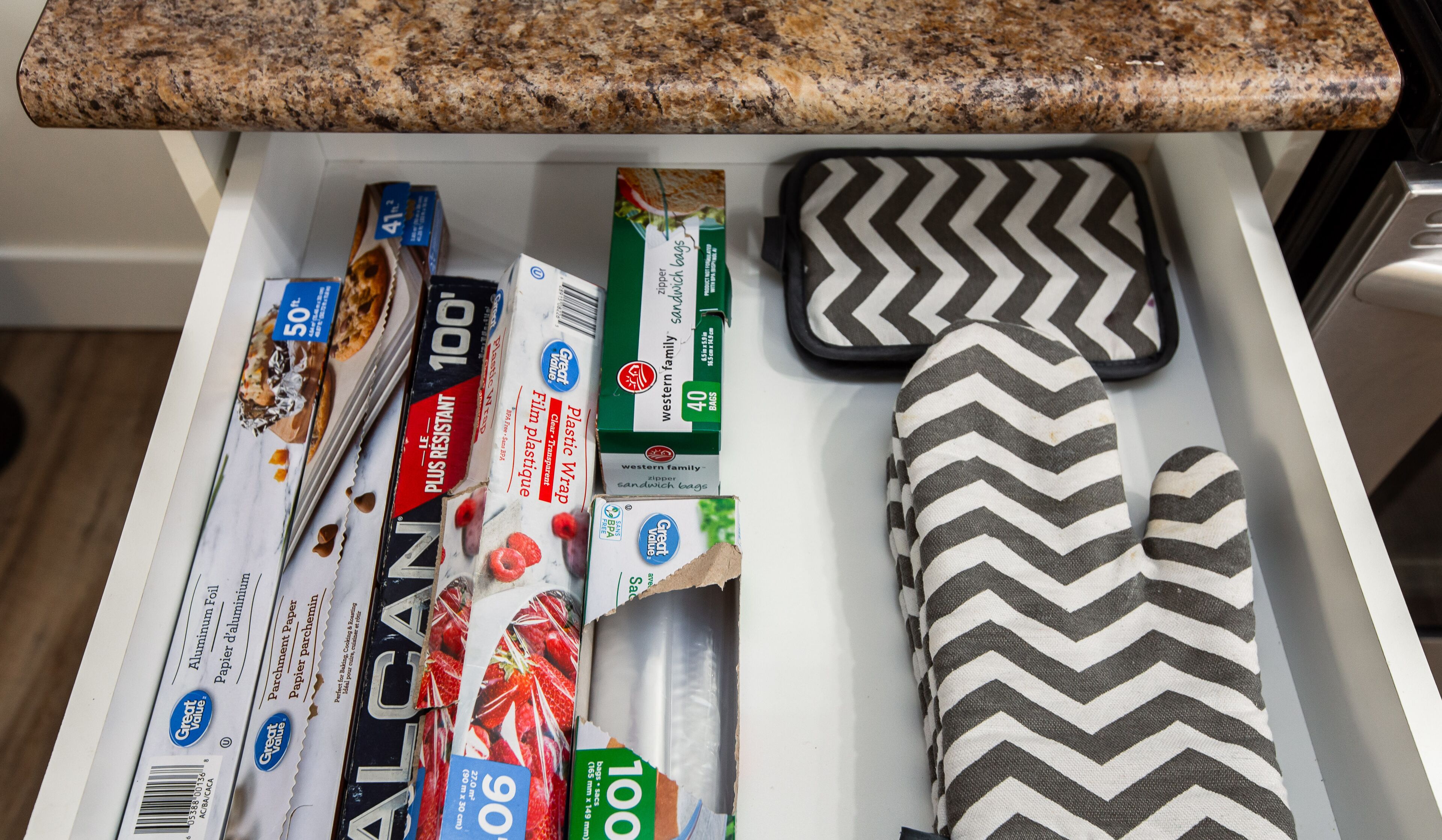 A kitchen drawer with various items including aluminum foil, plastic wrap, sandwich bags, and a patterned cloth.