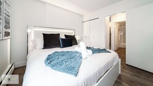 A modern hotel room with a large bed, white walls, and a wooden floor.
