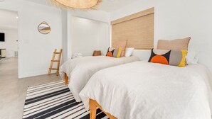 A modern bedroom with two beds, a large woven ceiling light, a wooden ladder, and a striped rug.